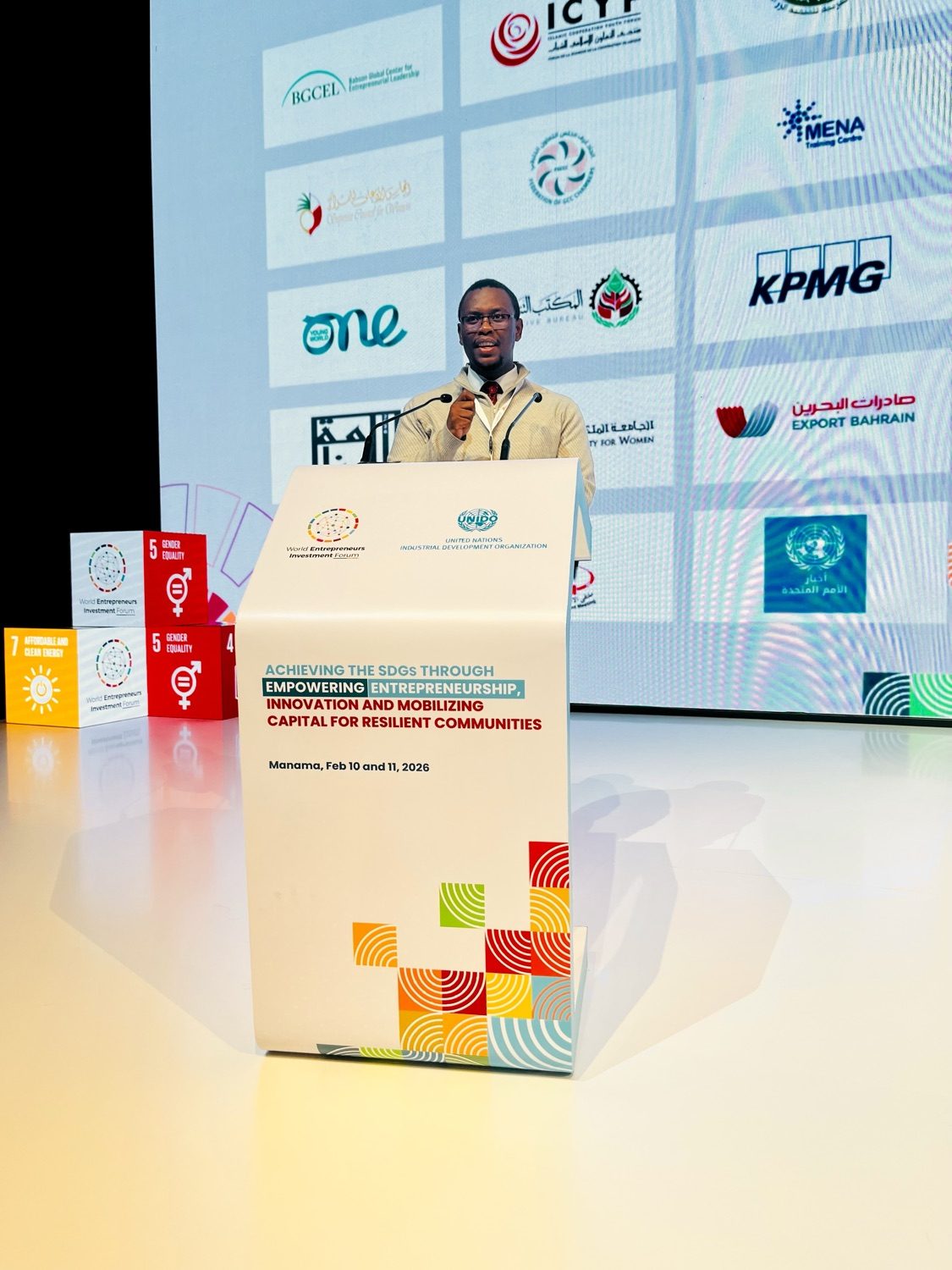 Olympus’s founder speaking at the World Entrepreneurs Investment Forum 2026 in Manama, at a podium marked with the forum’s theme
